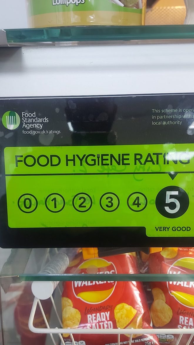 The food hygiene rating sticker in the cafe window, above a rack of crisps